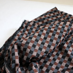 May include: Close-up of a fabric with a checkered pattern. The fabric features a repeating pattern of squares in black, brown, and gray. The fabric is folded, showing the texture and weave of the material. The edges of the fabric are frayed.