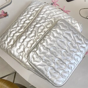 May include: Three white, quilted laptop sleeves with a heart pattern. The sleeves have a shiny, pearlescent finish and are stacked. The stitching creates a puffy, textured effect. The edges are neatly finished with a matching trim.
