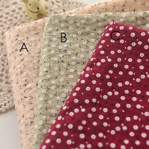 May include: Three fabric swatches with floral patterns. The swatches are in shades of peach, green, and red. Each fabric has a repeating pattern of small white flowers and tiny dark blue leaves.