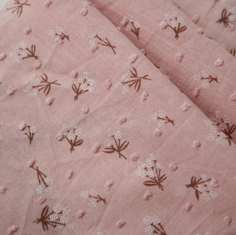 Op de afbeelding: Roze stof met een wit bloemenpatroon. De stof heeft een textuur van reli&euml;f stippen.