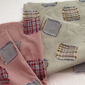 Könnte beinhalten: Nahaufnahme von zwei Stoffstücken mit einem rot-grünen Vichy-Muster. Jedes Stück hat mehrere karierte Flicken mit ausgefransten Kanten. Die Flicken sind in verschiedenen Farben gehalten, darunter Rot, Blau und Schwarz.