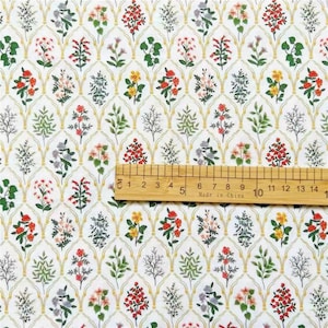 May include: White fabric with a repeating pattern of yellow, red, and green floral designs. The fabric is measured with a ruler in inches.