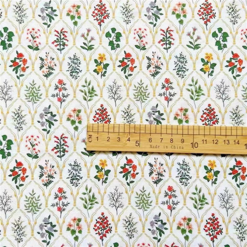 May include: White fabric with a repeating pattern of yellow, red, and green floral designs. The fabric is measured with a ruler in inches.