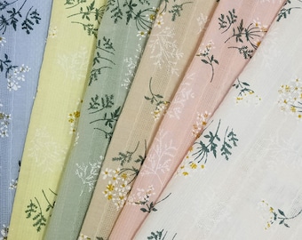 Op de afbeelding: Een assortiment stoffen stalen in verschillende pastelkleuren, waaronder blauw, geel, groen, beige en roze. Elke stof heeft een delicaat bloemenpatroon met witte en gele accenten, wat een zachte en luchtige uitstraling creëert.