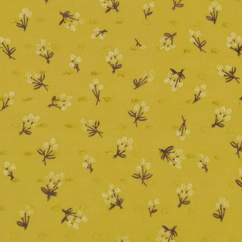 Op de afbeelding: Een gele stof met een wit en bruin bloemenpatroon. De stof heeft een textuur.