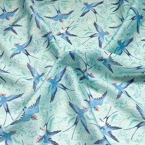 May include: A light blue fabric with a repeating pattern of blue birds with red accents, set against a backdrop of white flowers and green foliage. The birds are depicted in flight, creating a dynamic and airy feel.