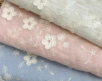 May include: Three folded layers of fabric in light sage green, dusty rose, and soft blue. Each layer features a delicate white floral embroidery pattern with detailed petals and leaves stitched across the textured, semi-sheer material surface.