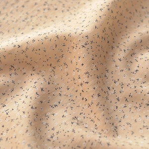 May include: Close-up of a beige fabric with a delicate floral pattern. The fabric has small, dark blue and white floral accents scattered across its surface. The material appears soft and slightly textured, with subtle folds.