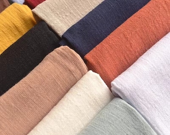 May include: A collection of folded fabric swatches featuring a textured, woven surface. The assortment includes various colors such as white, light gray, beige, peach, mustard yellow, black, dark blue, terracotta, and deep red, arranged in layers.