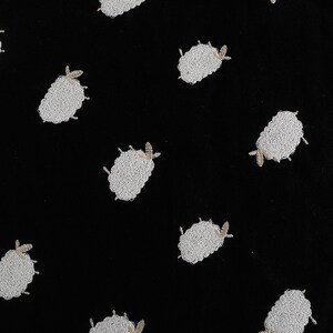 Puede incluir: Tela negra con un patr&oacute;n repetido de ovejas bordadas en blanco.
