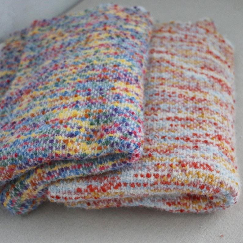 May include: Two folded pieces of textured knit fabric. The left piece features a dense, multicolored speckled pattern of blue, yellow, red, and purple. The right piece displays a lighter, horizontal-striped pattern of orange, red, and white.