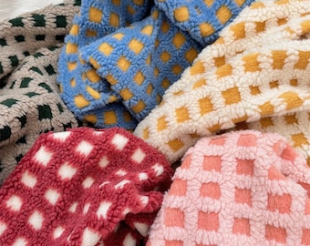 May include: A collection of soft, fuzzy fabric pieces featuring a repeating grid pattern. The fabric comes in various colors including blue with yellow squares, cream with yellow squares, red with white squares, and pink with white squares.