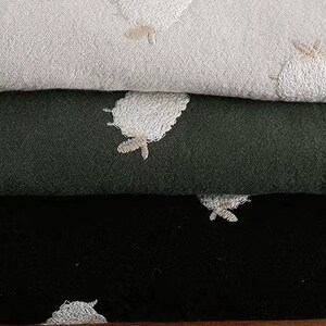 Puede incluir: Tres capas de tela con dise&ntilde;os de ovejas bordadas. La capa superior es beige claro, la capa intermedia es verde oscuro y la capa inferior es negra.