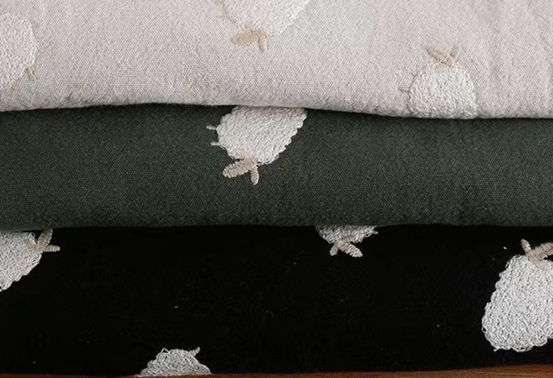 Puede incluir: Tres capas de tela con dise&ntilde;os de ovejas bordadas. La capa superior es beige claro, la capa intermedia es verde oscuro y la capa inferior es negra.