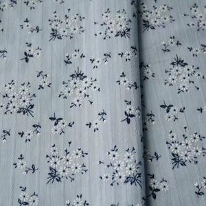 K&ouml;nnte beinhalten: Ein hellblauer Stoff mit einem wei&szlig;en Blumenmuster. Der Stoff hat eine subtile gestreifte Textur.