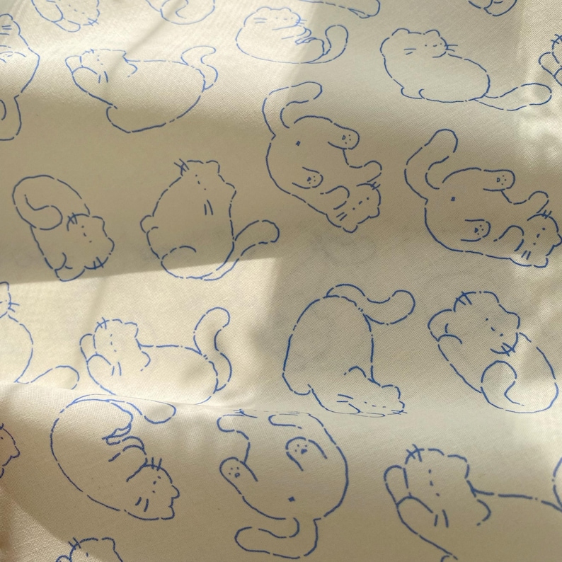 May include: Off-white fabric with a repeating pattern of blue cat illustrations. The cats are depicted in various playful poses, with simple line drawings creating a whimsical design. The fabric has a soft, slightly textured appearance.