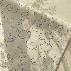 May include: White fabric with a repeating pattern of blue cat illustrations in various poses. The cats are drawn with simple outlines, creating a playful and whimsical design. The fabric appears to be soft and lightweight.