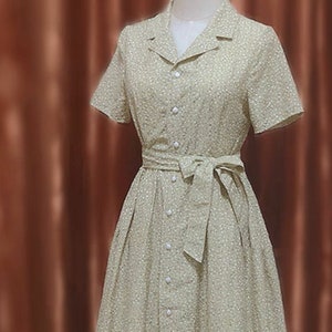 May include: A light green button-down dress with a small white polka dot pattern. The dress features short sleeves, a collared neckline, and a matching fabric belt tied at the waist. The dress is displayed on a mannequin.