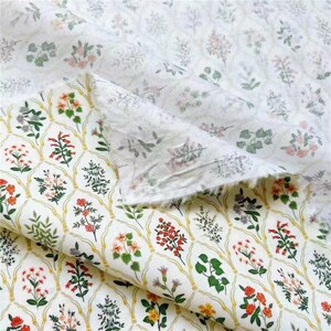 May include: White cotton fabric with a floral print. The fabric features a repeating pattern of small flowers and leaves in shades of pink, red, green, and yellow. The fabric is folded in half, revealing the back side of the fabric, which is a solid white.