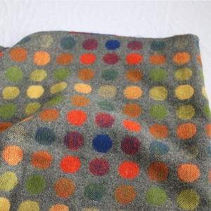 Può includere: Un tessuto grigio con un motivo ripetuto di pois colorati. I pois sono in tonalità di arancione, rosso, giallo, verde e blu. Il tessuto sembra essere tessuto, con una superficie leggermente strutturata.
