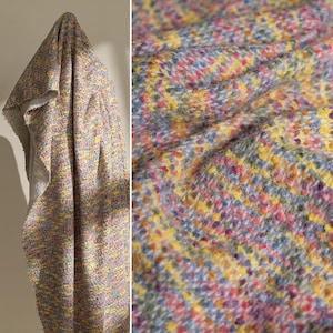 May include: A textured fabric featuring a multi-colored speckled pattern with vibrant hues of yellow, pink, blue, and purple. The material has a soft, fuzzy surface with a woven appearance, showing a dense arrangement of small, colorful dots.