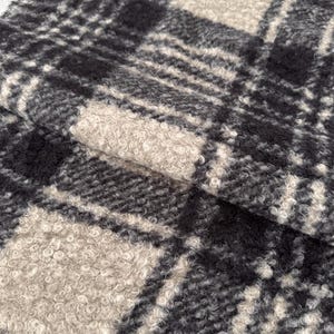 May include: A textured fabric featuring a black and beige plaid pattern. The material has a thick, curly, and looped pile surface that creates a distinct tactile appearance with alternating dark and light squares arranged in a grid formation.