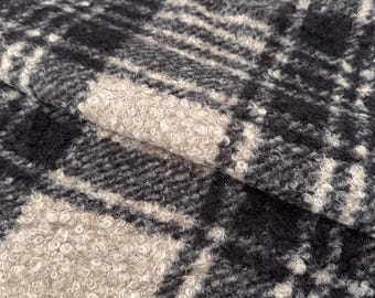 May include: A textured fabric featuring a black and beige plaid pattern. The material has a thick, curly, and looped pile surface that creates a distinct tactile appearance with alternating dark and light squares arranged in a grid formation.