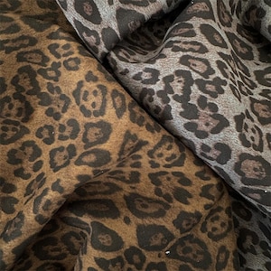 Puede incluir: Dos piezas de tela con estampado de leopardo. Una pieza es de color marrón cálido con manchas de color marrón oscuro, mientras que la otra es de color gris frío con manchas de color gris oscuro. Ambas telas tienen un aspecto suave y texturizado.