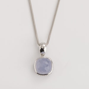 May include: A silver necklace with a square, light blue pendant. The pendant has a faceted surface and is set in a silver frame. The chain is a thin, snake chain style, and the background is white.