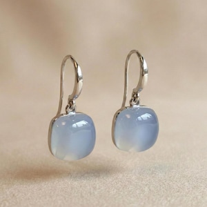 Peut inclure: Une paire de boucles d'oreilles pendantes argentées. Chaque boucle d'oreille présente une pierre précieuse carrée bleu pâle sertie dans un cadre argenté. Les boucles d'oreilles ont un design simple et élégant.