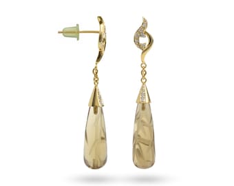 Puede incluir: Un par de pendientes colgantes dorados con una piedra preciosa marrón claro en forma de lágrima. Los pendientes presentan un diseño de remolino decorativo con pequeñas piedras transparentes y cierre de tuerca. Las piedras preciosas tienen patrones grabados.
