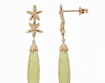 Puede incluir: Pendientes colgantes dorados con diseño floral, con dos acentos de flores y pequeñas piedras transparentes. Los pendientes tienen un colgante de piedra en forma de lágrima verde claro con detalles tallados. Se muestran sobre un fondo blanco.