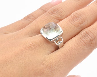 May include: A silver ring with a large, clear, faceted gemstone. The ring has a simple band and a square-shaped setting.