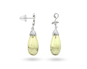 Puede incluir: Un par de pendientes colgantes plateados con gemas amarillas pálidas en forma de pera. Los pendientes tienen un diseño floral y una textura acanalada. Se presentan sobre un fondo blanco, resaltando su elegancia.
