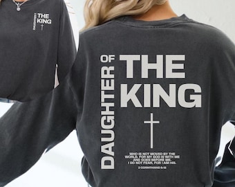May include: A charcoal gray long-sleeved shirt with the text "Daughter of the King" and a cross on the back. The text "Who is not moved by the world. For my God is with me and goes before me. I do not fear, for I am His. 2 Corinthians 6:16" is printed below the cross.
