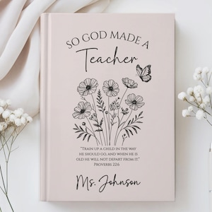 May include: A light pink journal with the text "SO GOD MADE A Teacher" and a floral illustration. The journal also includes the quote "TRAIN UP A CHILD IN THE WAY HE SHOULD GO, AND WHEN HE IS OLD HE WILL NOT DEPART FROM IT." and "Ms. Johnson".