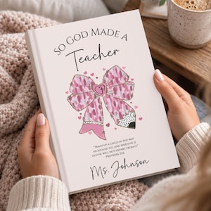 Op de afbeelding: Een wit hardcover boek met de titel So God Made A Teacher met een roze gestreepte strik-afbeelding met een hart met een kruis, kleine roze hartjes, een potloodpunt en de tekst Train up a child in the way he should go, en Ms. Johnson.