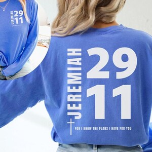 Op de afbeelding: Een langarm, lichtblauw T-shirt met witte tekst op de rug. De tekst luidt "Jeremia 29:11" en "Want ik weet welke plannen ik voor jullie heb".