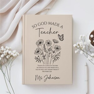 May include: A beige journal with the text "SO GOD MADE A Teacher" and a floral illustration. The journal also includes the quote "TRAIN UP A CHILD IN THE WAY HE SHOULD GO, AND WHEN HE IS OLD HE WILL NOT DEPART FROM IT." and the name "Ms. Johnson."