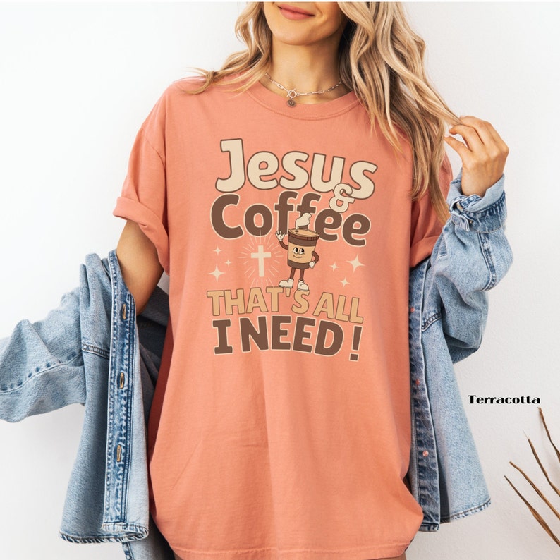 May include: A terracotta colored t-shirt with the text "Jesus & Coffee That's All I Need!" in brown and white lettering. A cartoon coffee cup with a cross is in the center of the design.