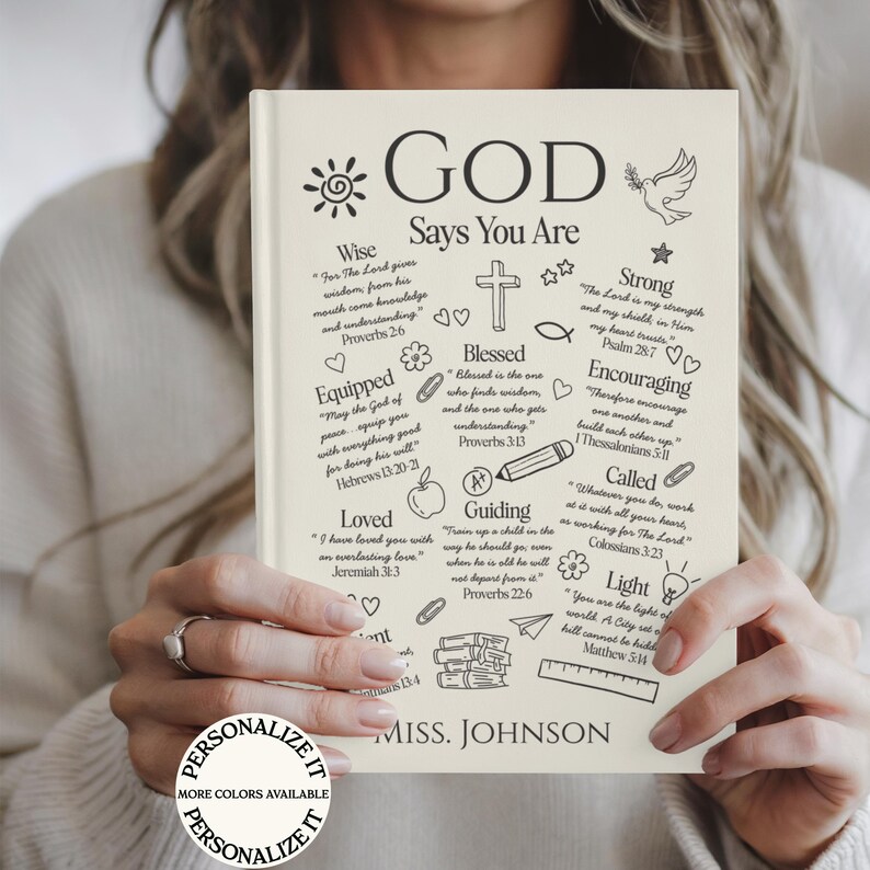May include: A cream-colored journal with the words "GOD Says You Are" in black. The journal is decorated with various illustrations and inspirational quotes. The name "MISS. JOHNSON" is printed at the bottom. The words "PERSONALIZE IT" are also visible.