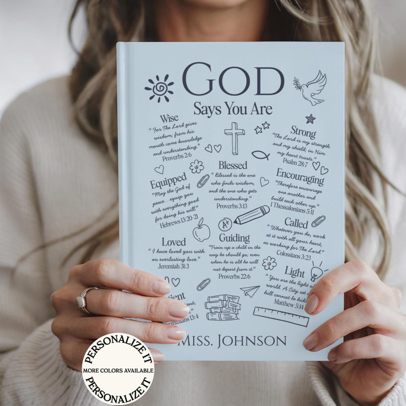 May include: A light blue journal with the words "GOD Says You Are" and inspirational text. The journal features a variety of illustrations and the name "MISS. JOHNSON" at the bottom. A button that says "PERSONALIZE IT" is in the lower left corner.