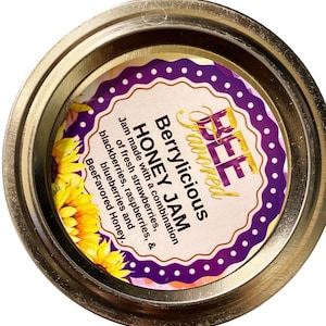 May include: A jar of Bee Favored Berrylicious Honey Jam. The label features text and a purple border with white dots. The jam is made with strawberries, raspberries, blackberries, and blueberries.