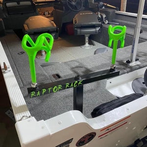 May include: A boat interior with a gray carpeted floor and black seats. The boat features a black metal Raptor Rack with two neon green rod holders. The text "RAPTOR RACK" is visible on the rack.