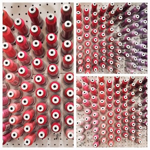 May include: A wall display of spools of thread in various shades of red, pink, and purple. The spools are arranged in a heart shape.