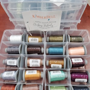 May include: A clear plastic storage container with 12 spools of metallic embroidery floss. The spools are arranged in rows of four. The container has a label that reads "Kimberbell Happy Hoop Decor Christmas Nativity Ornaments".