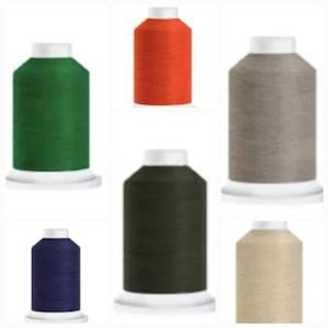 May include: A collection of six spools of thread in various colors, including green, orange, gray, navy blue, dark green, and beige. Each spool has a white base and cap, and the thread is tightly wound around the spool.