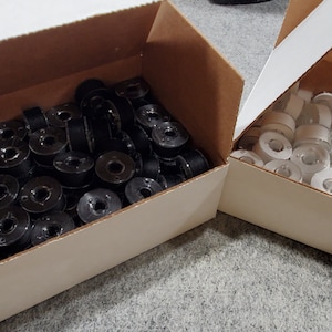 May include: Two cardboard boxes filled with spools of thread. One box contains black thread spools and the other contains white thread spools.