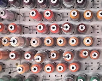 Peut inclure: Une collection de bobines de fil colorées, disposées sur un panneau perforé blanc. Les bobines présentent une variété de couleurs, notamment des nuances de rose, d'orange, de jaune, de vert et de violet. Chaque bobine est fixée avec une épingle métallique.