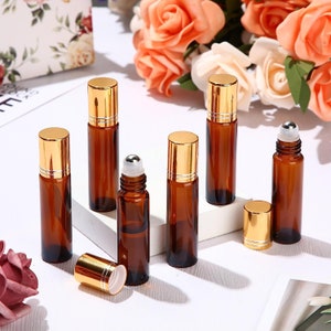 May include: A set of seven amber glass roller bottles with gold lids. The bottles are arranged on a white surface. The bottles are all the same size and shape, and they have a roller ball applicator.
